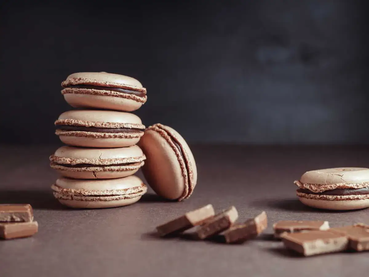 Une pile de macarons de Noël à la garniture chocolatée, avec des morceaux de chocolat sur le côté.