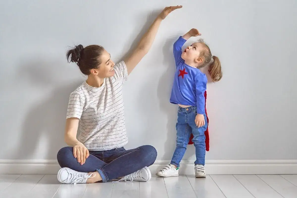 Mama mierzy, ile dziecko rosnie w rok. Mała superbohaterka próbuje sięgnąć jak najwyżej.