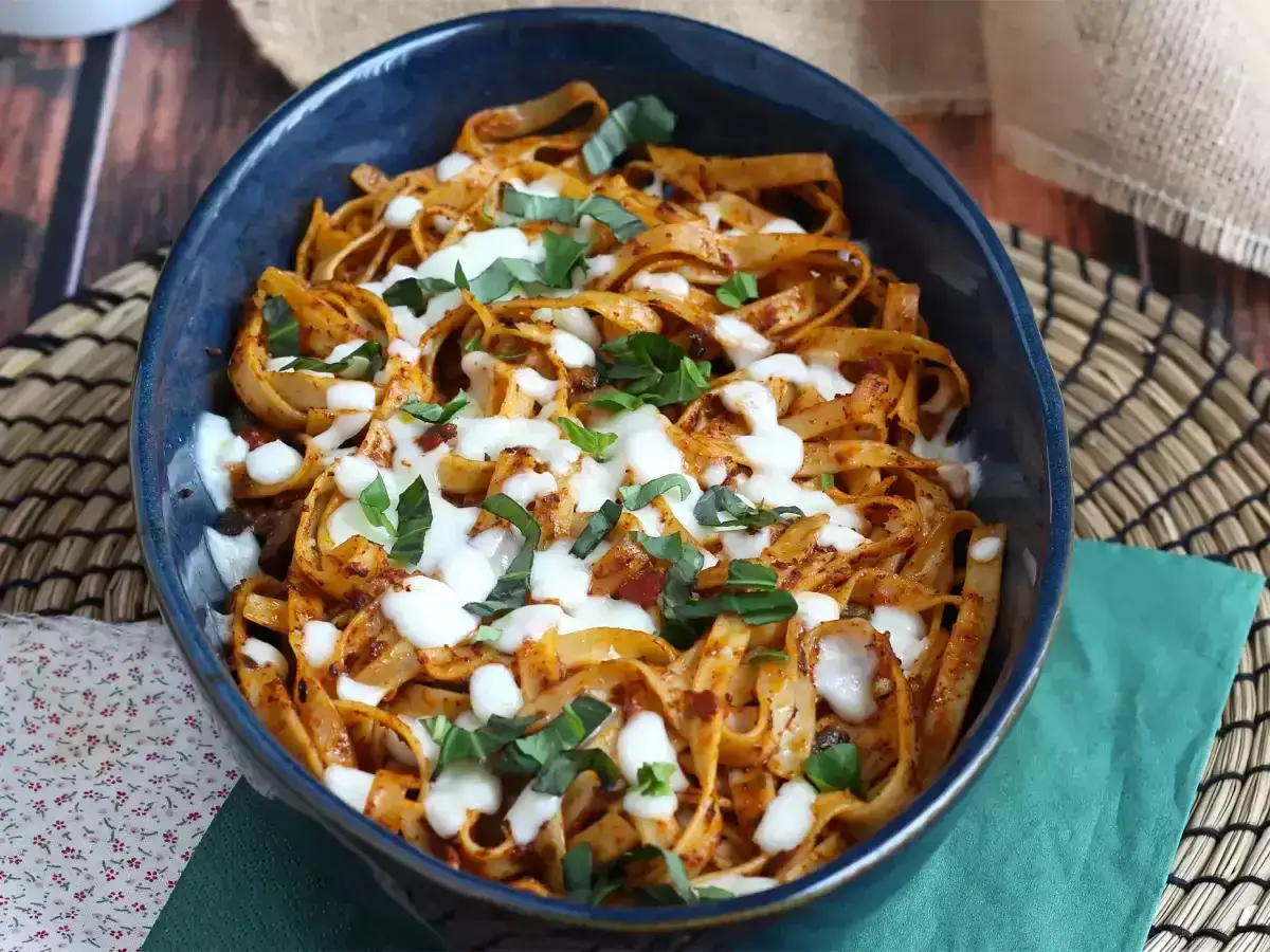 Makaron tagliatelle w sosie pomidorowym z mozzarellą i bazylią w niebieskiej misce.