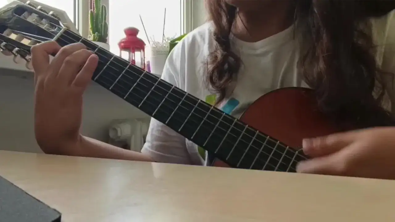 Osoba gra na gitarze klasycznej, ćwicząc znane utwory na gitarę klasyczną.
