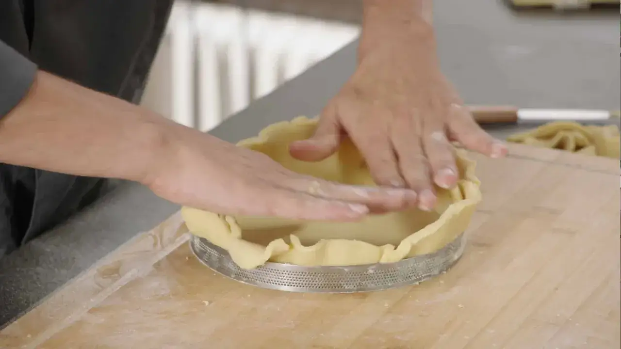Mains expertes pour foncer une pâte dans un cercle à tarte. La pâte est étalée et ajustée sur les bords.