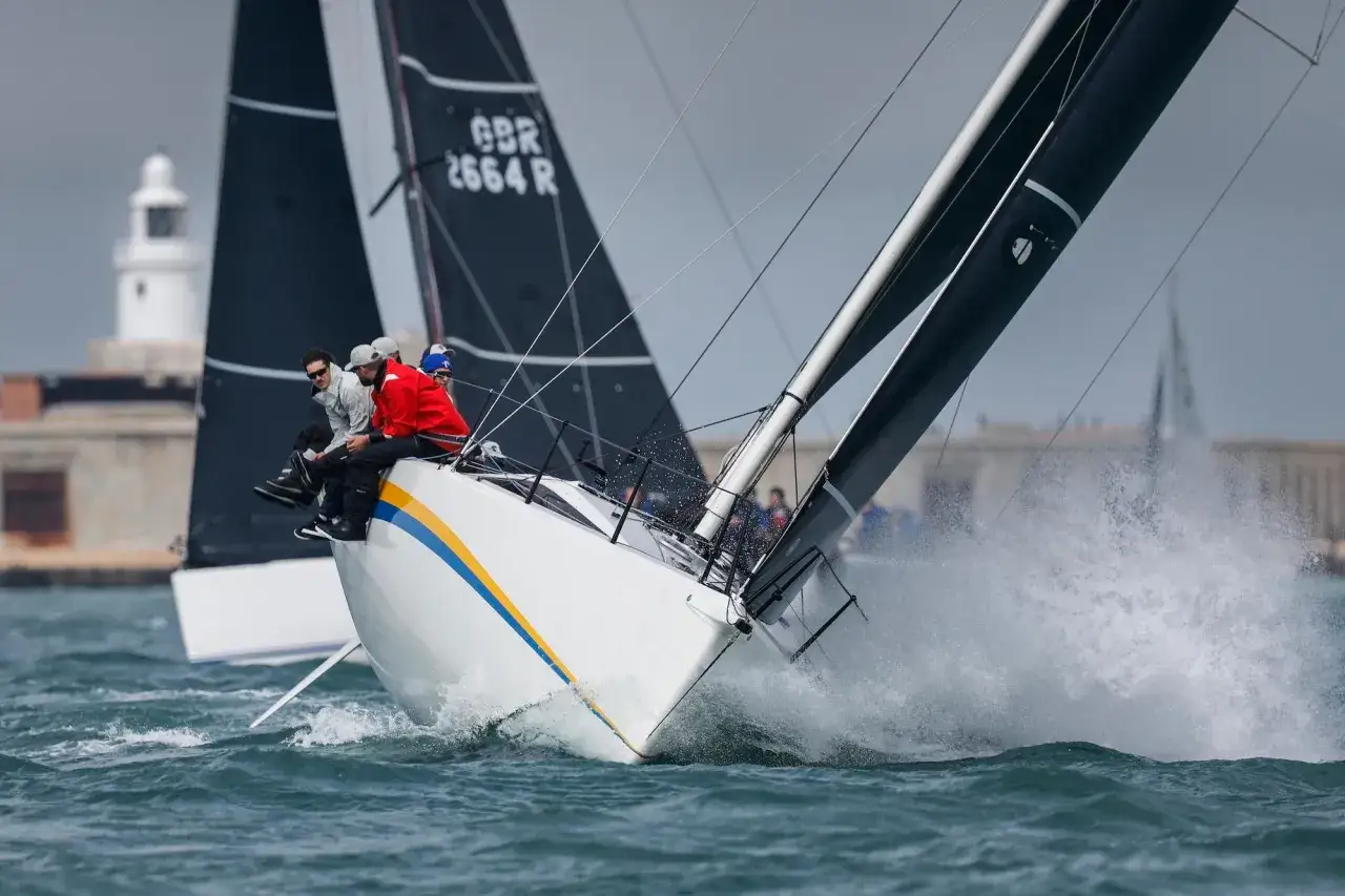 Segelboote kämpfen bei der Admirals Cup Regatta um die Wette. Gischt spritzt, die Crew sitzt tief.