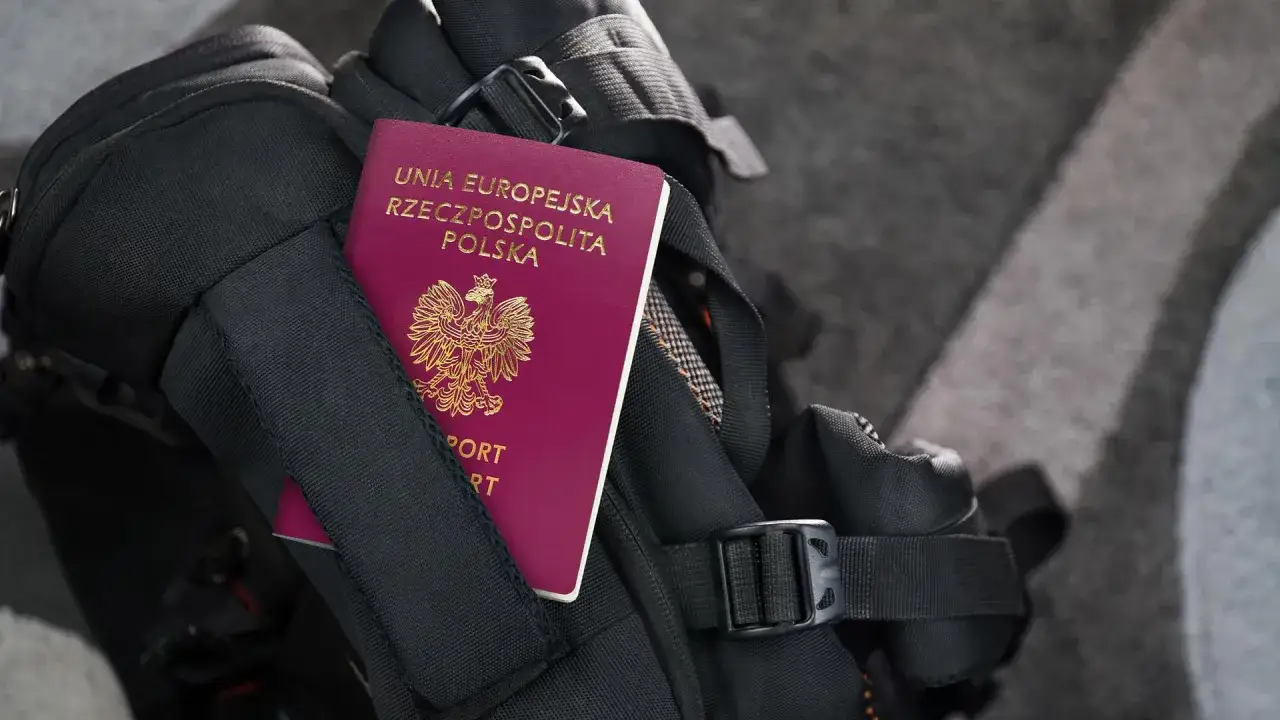 Polski paszport wpięty w czarny plecak podróżny.
