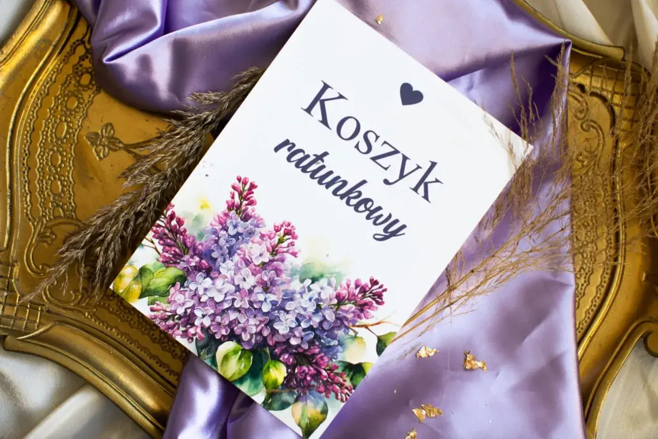 Eleganckie elementy zaproszenia: kartka z napisem "Koszyk ratunkowy", ozdobiona bukietem bzu, na tle fioletowej satyny i złotej ramki.