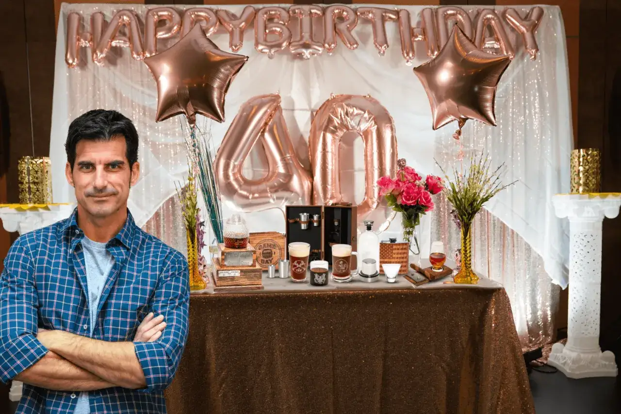 Mężczyzna w kratę stoi przed stołem z prezentami i balonami z napisem "Happy Birthday 40".