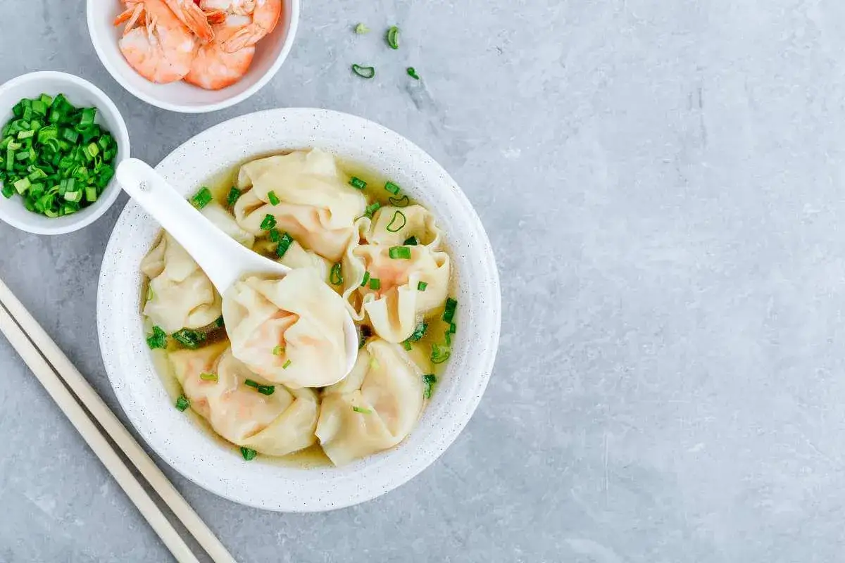 Aksamitna zupa wonton z krewetkami i szczypiorkiem, podana z pałeczkami.