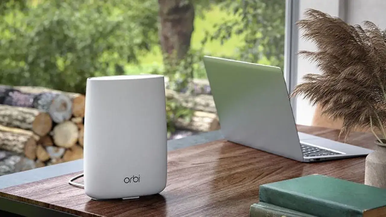 Ein weißer Orbi WLAN-Router steht neben einem Laptop auf einem Holztisch.