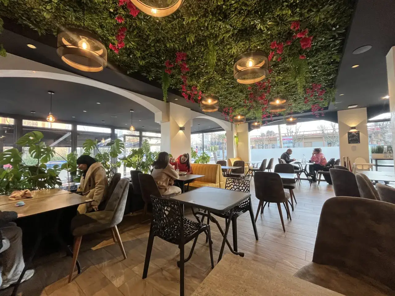 Intérieur d'un bar à desserts avec plafond végétalisée, lumières suspendues et tables occupées.
