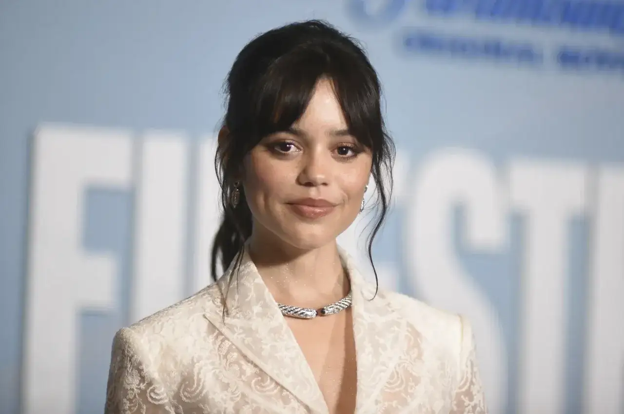 Jenna Ortega, uśmiechnięta, w białej koronkowej marynarce i efektownej biżuterii. Czy Jenna Ortega żyje? Tak, wygląda świetnie!