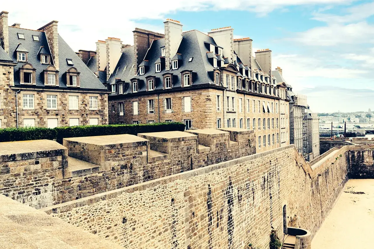Murs de pierre de la ville fortifiée de Saint-Malo, avec des maisons bretonnes typiques et une vue sur la mer. Imaginez une pause à la taverne de Saint-Malo.