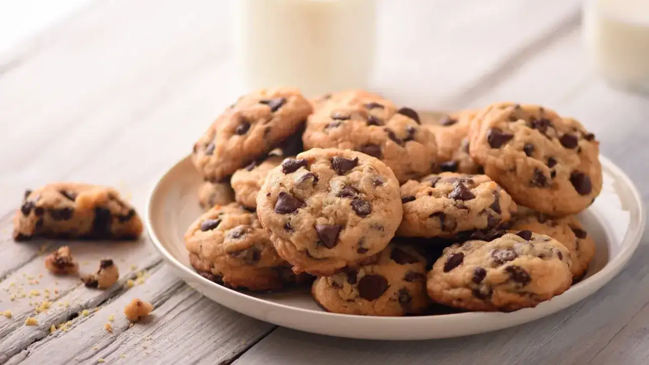 Une assiette de délicieux cookie fait maison, parsemés de pépites de chocolat, avec un verre de lait en arrière-plan.