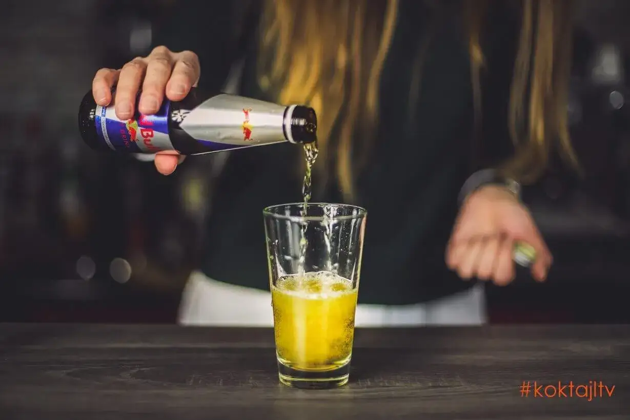 Osoba nalewa do szklanki drink z red bullem.