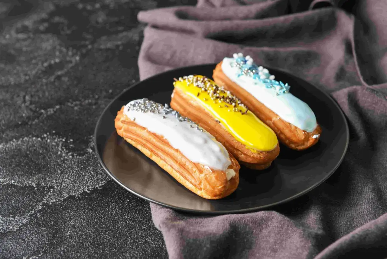 Trois éclairs colorés, fruits d'une recette pâte à choux réussie, sur une assiette noire.