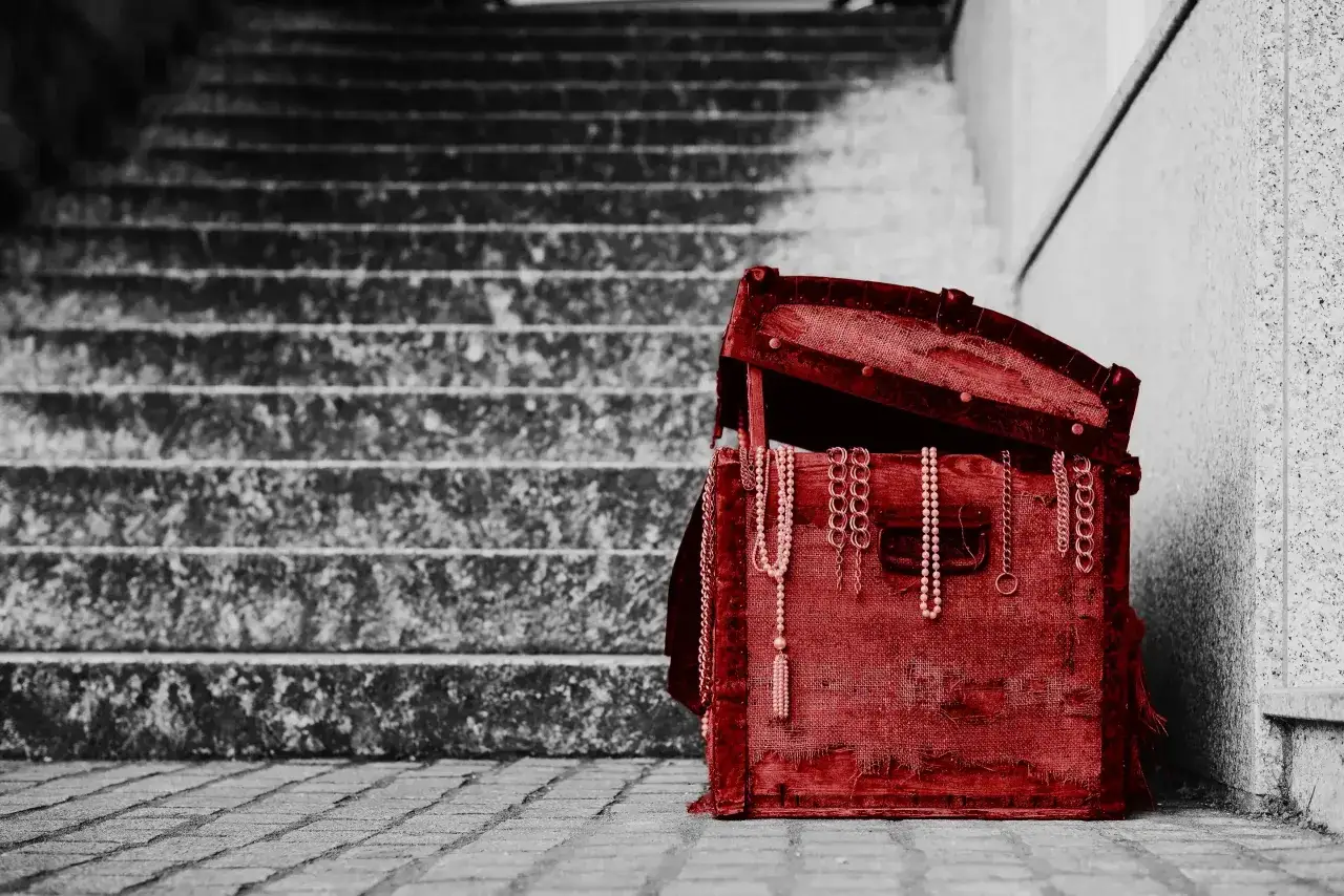 Czerwona skrzynia z biżuterią, stojąca na schodach. To pamiątka, spadek po rodzicach, pełen wspomnień.