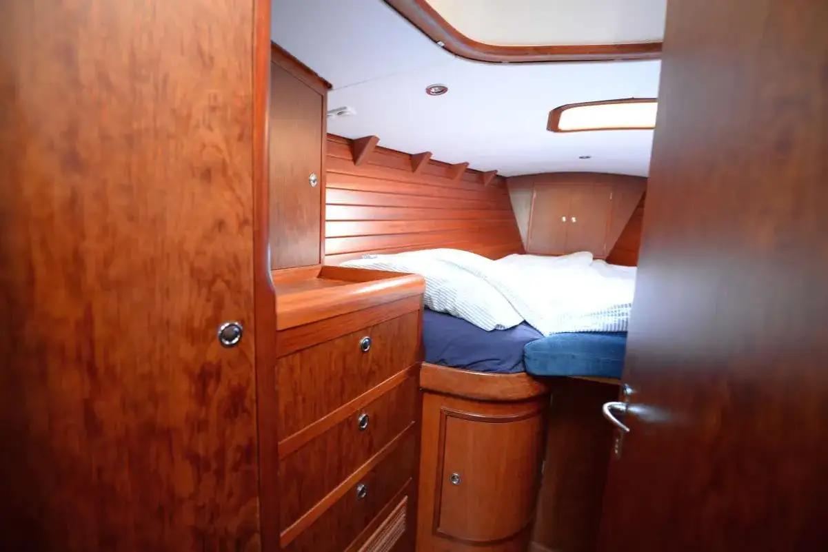 Gemütliches Bett mit gestreifter Bettwäsche im Innenbereich einer Segelyacht. Holzverkleidung und Schränke schaffen eine warme Atmosphäre.