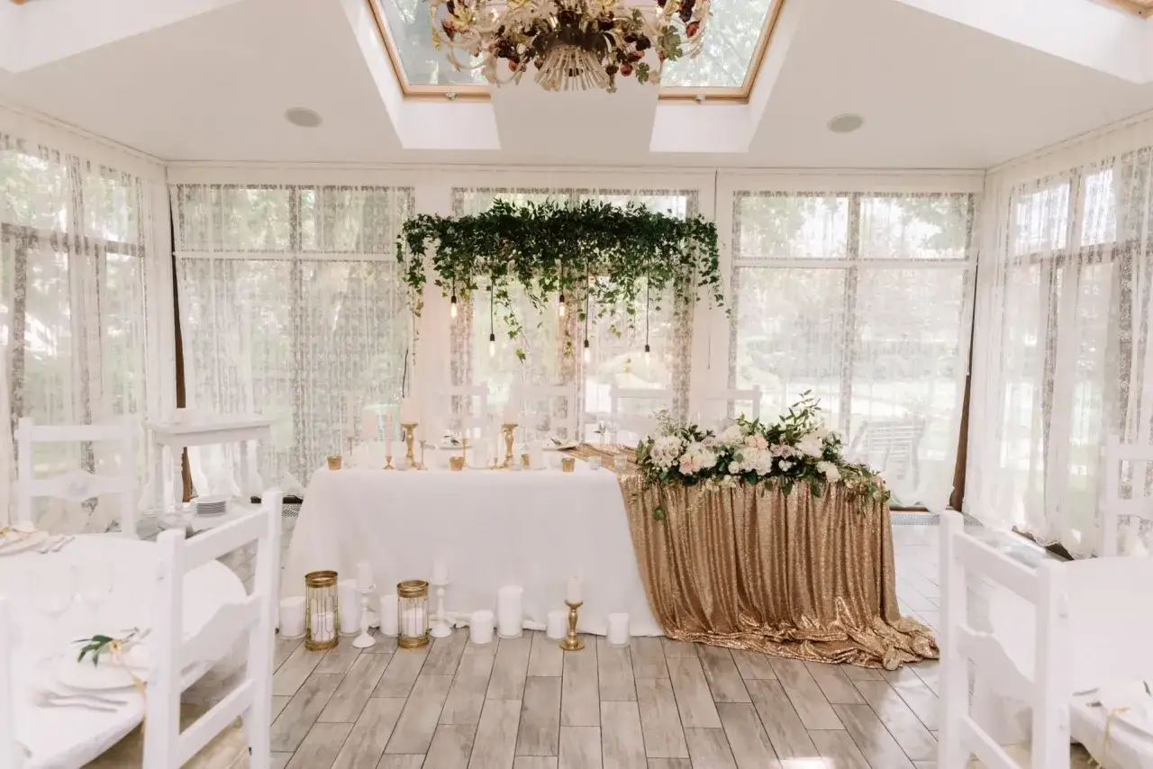 Elegancka sala weselna z białymi krzesłami i stołem pary młodej ozdobionym złotymi cekinami i kwiatami. Wspaniałe kolory na wesele.