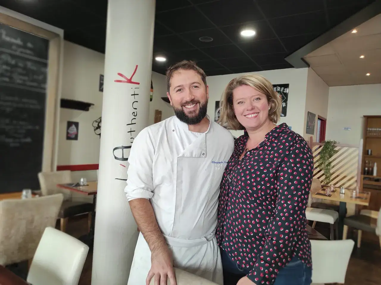 Le chef et sa collègue sourient devant la colonne "Authentik St Grégoire". L'ambiance chaleureuse du restaurant est palpable.