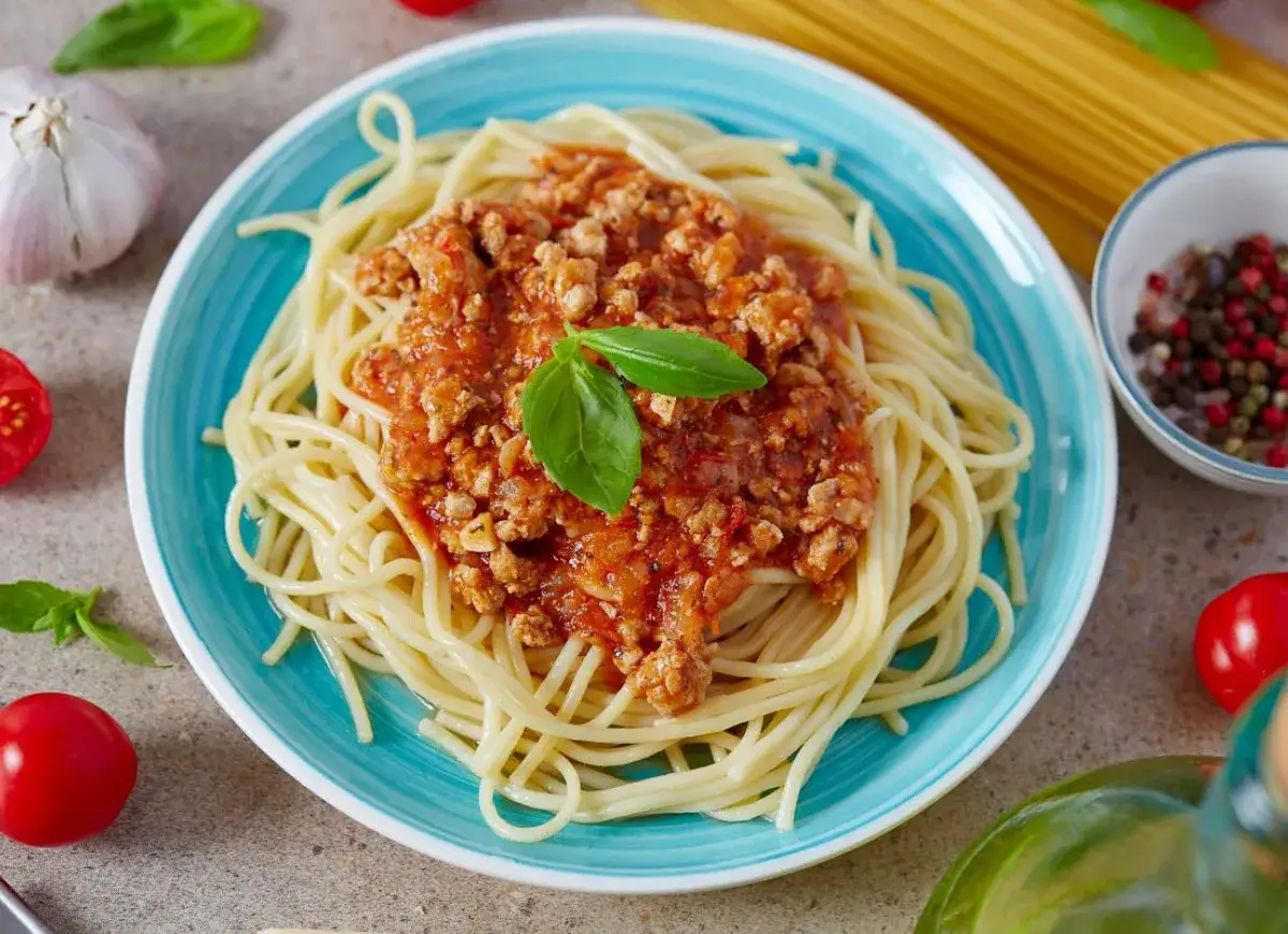 Pyszne spaghetti z sosem bolońskim, idealne, gdy zastanawiasz się, jak zrobić sos do spaghetti. Podane na niebieskim talerzu, z bazylią i pomidorkami.