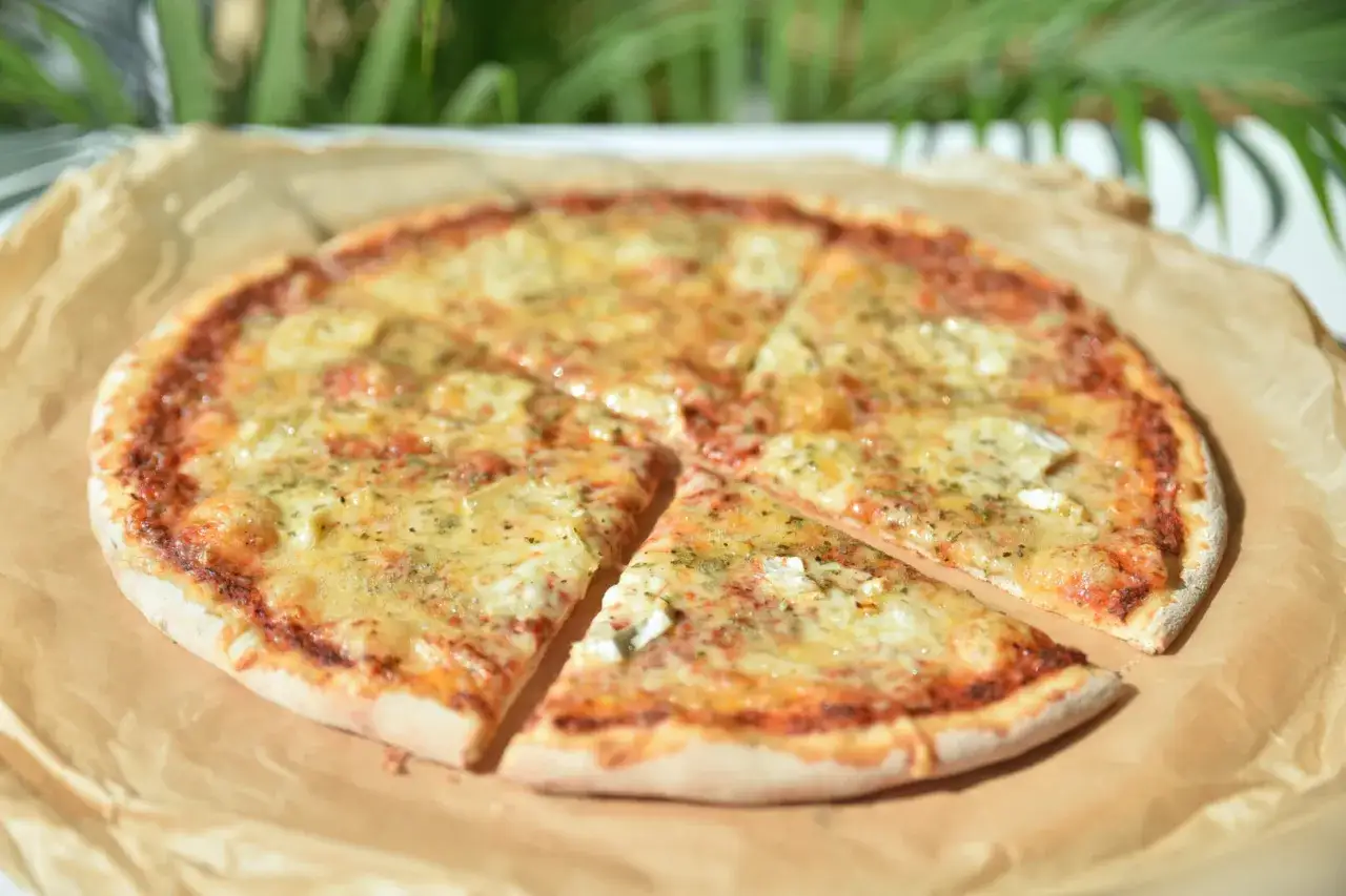Pizza 4 sery z roztopionym serem i ziołami na papierze do pieczenia.