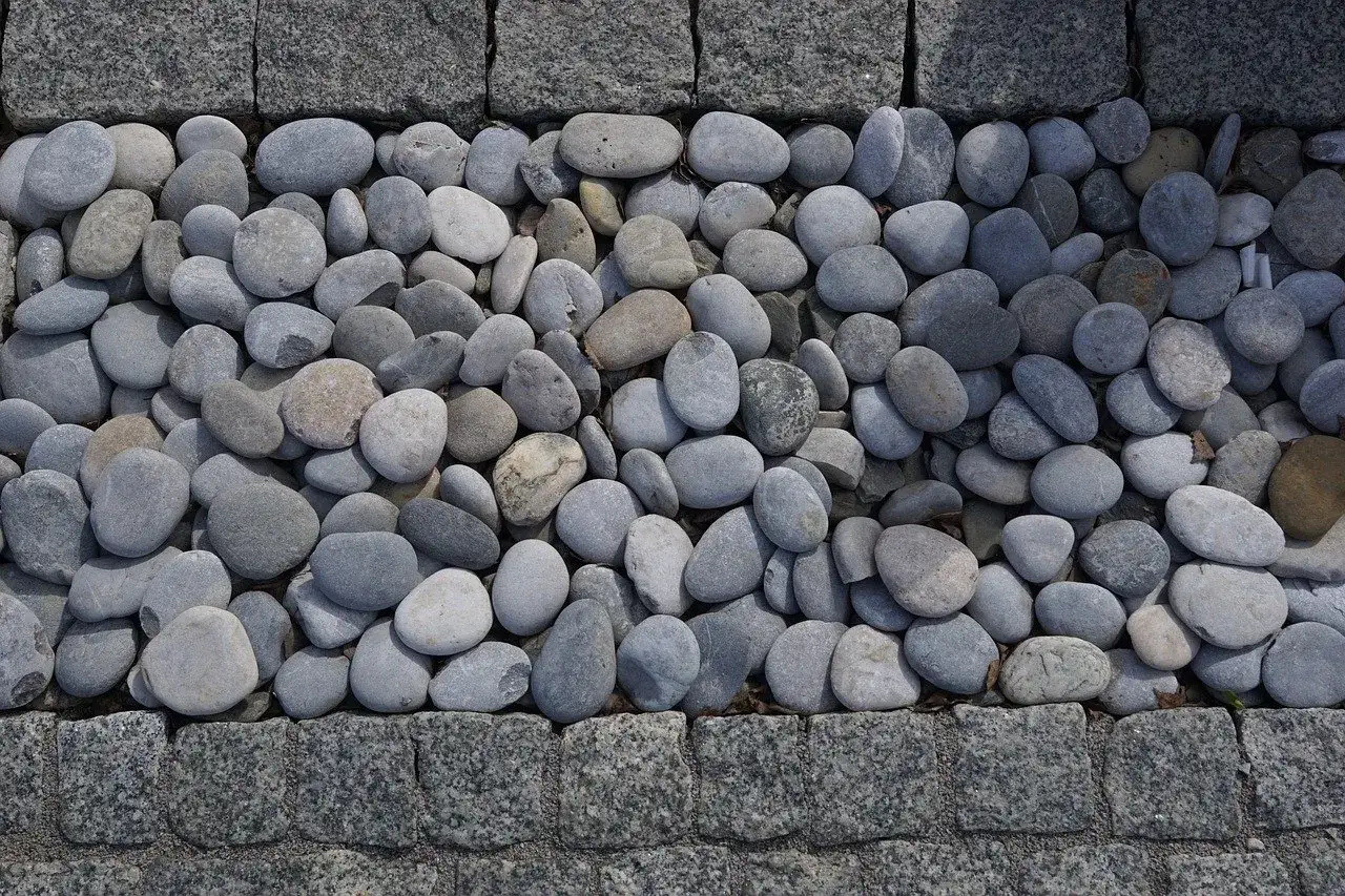 Gładkie, szare kamienie tworzą naturalną dekorację w ogrodzie, otoczone granitową kostką.