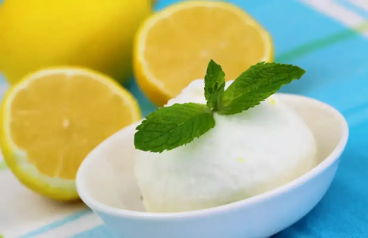 Crème glacée citron rafraîchissante, garnie de menthe fraîche, avec des citrons coupés en arrière-plan.