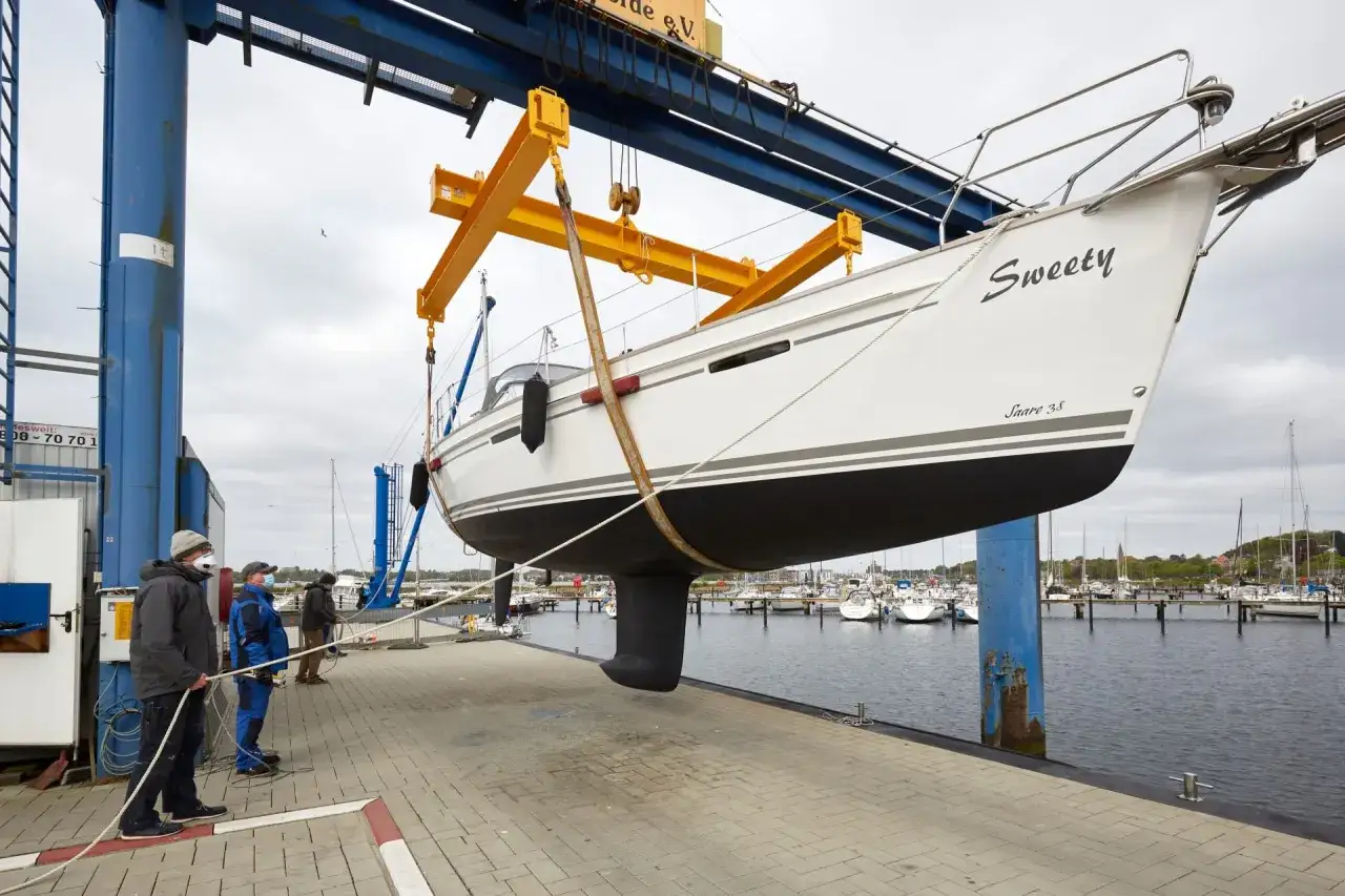 Segelboot "Sweety" wird für das unterwasserschiff reinigen aus dem Wasser gehoben. Männer sichern das Boot mit Seilen.