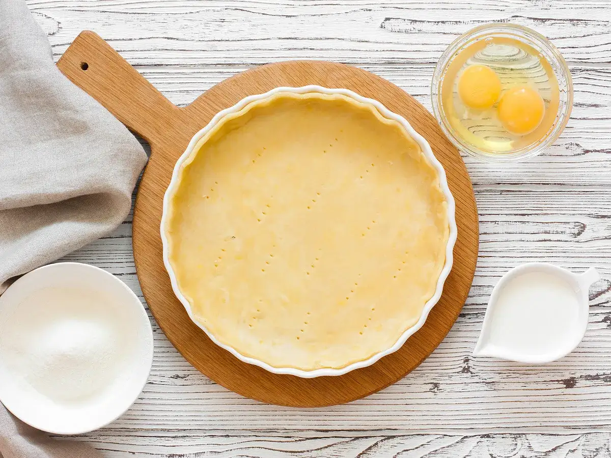 Préparation d'une pâte sucrée pour une tarte. Ingrédients : pâte dans un moule, œufs, sucre, lait.