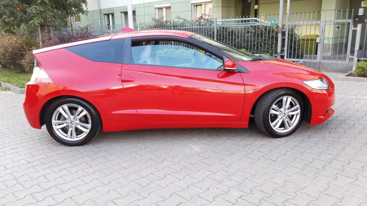 Czerwone Honda CRZ z czarnym dachem stoi na chodniku.