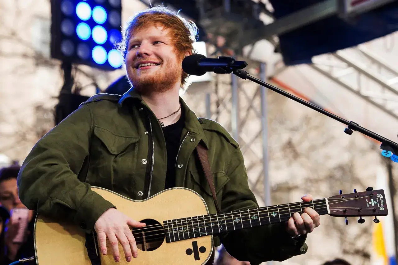 Ed Sheeran uśmiecha się, grając na gitarze akustycznej Martin.