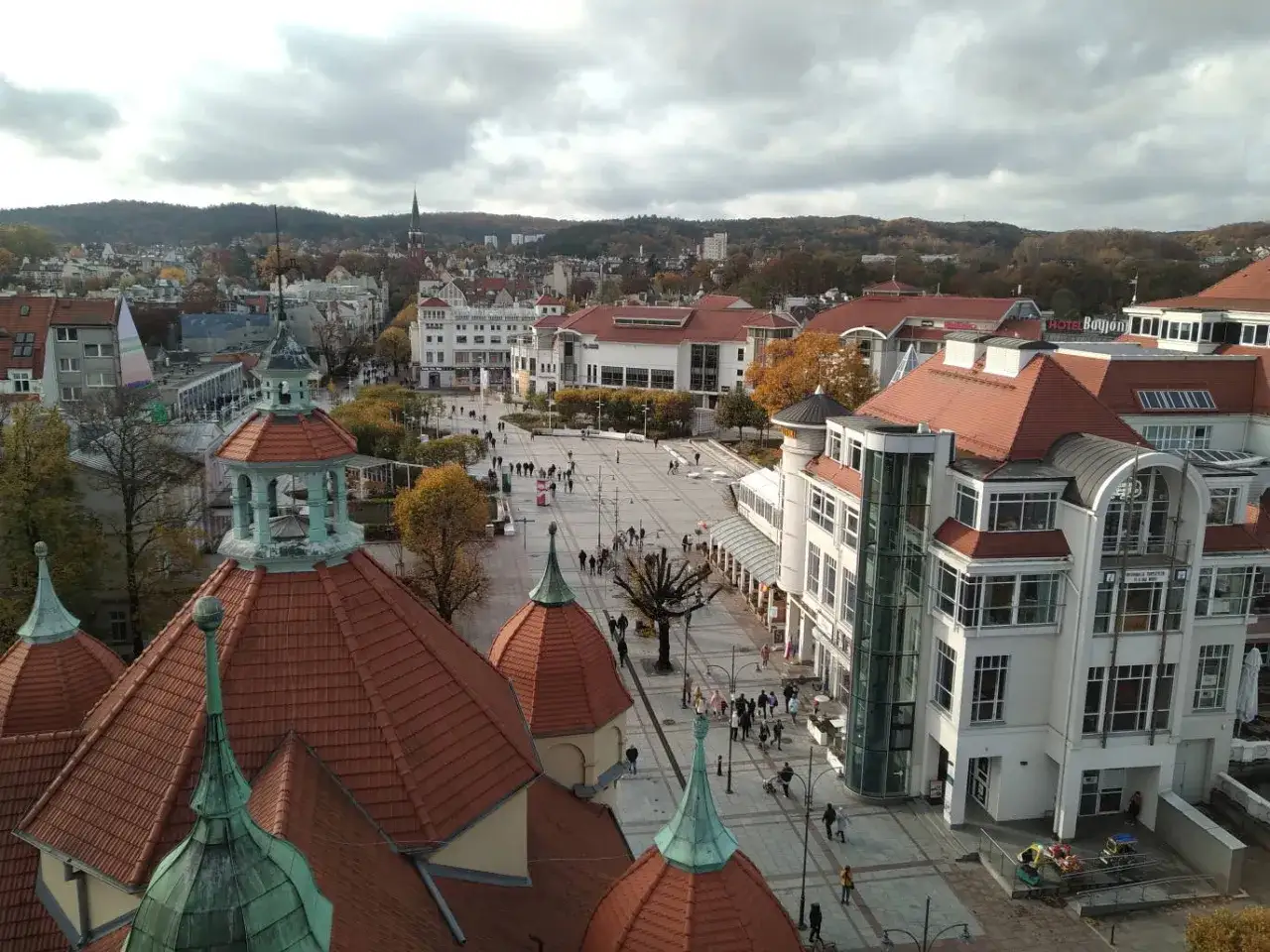 Widok na plac w Sopocie z charakterystycznymi dachami i budynkami. Wiele osób spaceruje, szukając sopotorium opinie.