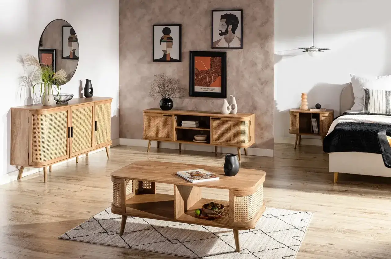 Jak zagospodarować róg pokoju salon? Drewniane meble z rattanowymi frontami, okrągłe lustro i grafiki na ścianie tworzą przytulną przestrzeń.