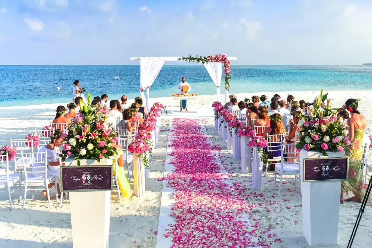 Plażowa ceremonia ślubna z różowymi płatkami kwiatów i błękitnym oceanem w tle. Idealne, nietypowe miejsce na wesele marzeń.