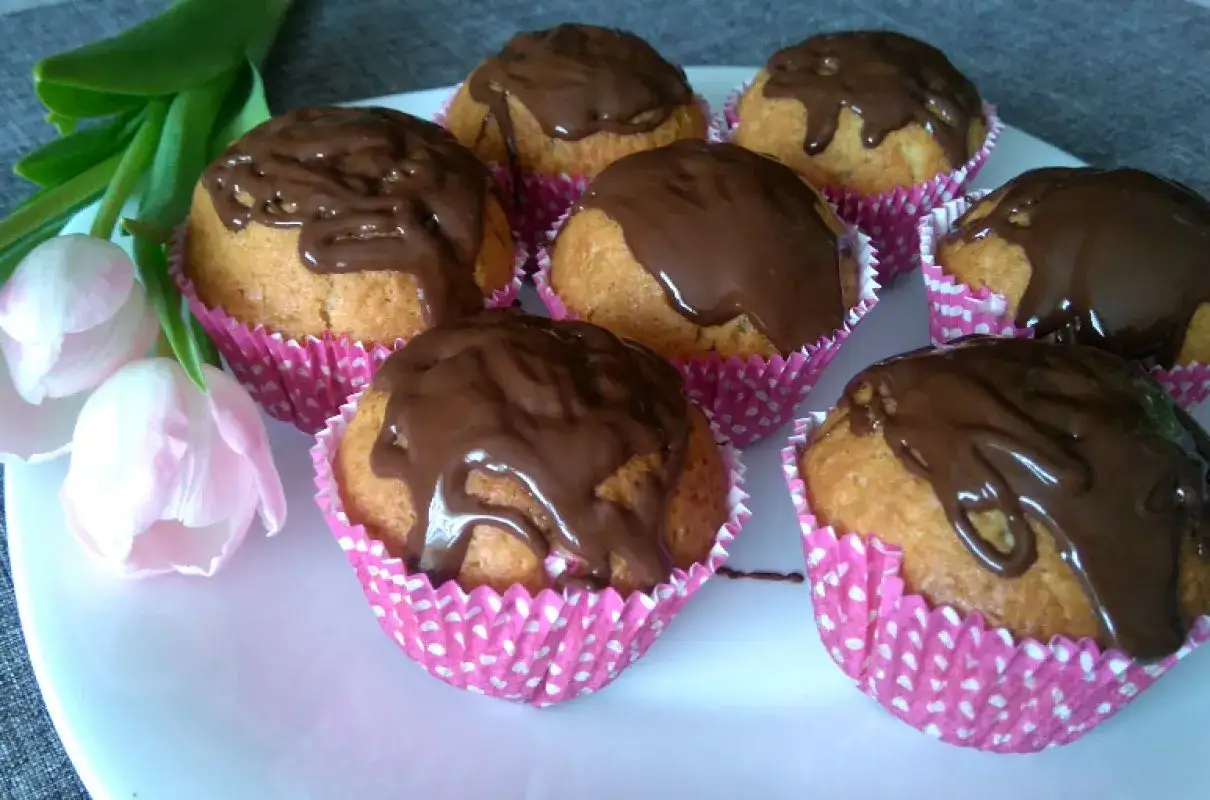 Pyszne muffiny z powidłami śliwkowymi, polane czekoladą, na talerzu z tulipanami.