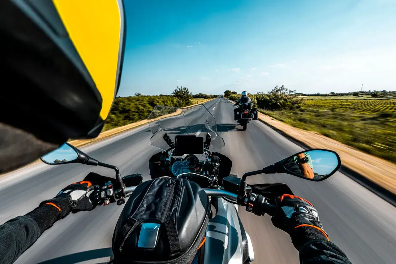 Przełęcz Salmopolska widziana z perspektywy motocyklisty. Droga wijąca się pośród zielonych pól, błękitne niebo i inny motocykl przed nami.