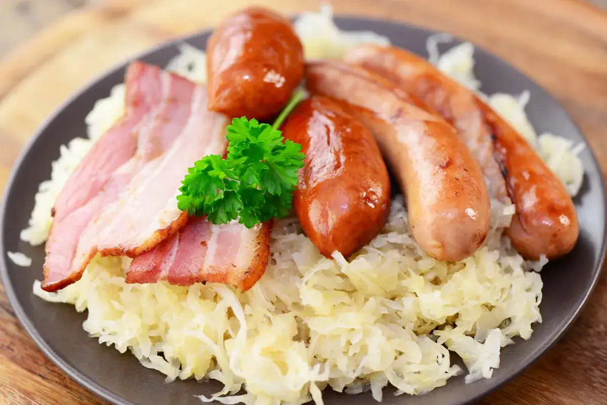 Assiette de choucroute allemande ou alsacienne garnie de saucisses et de lardons, décorée d'une touche de persil frais.