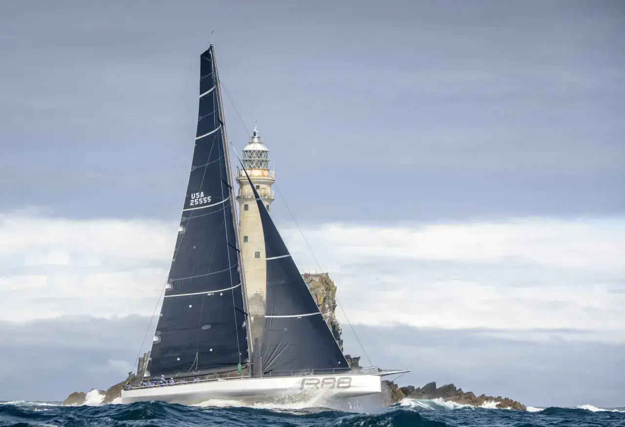 Segelboot mit schwarzen Segeln navigiert durch raue See am Fastnet Rock, ein dramatischer Moment im Fastnet Race.