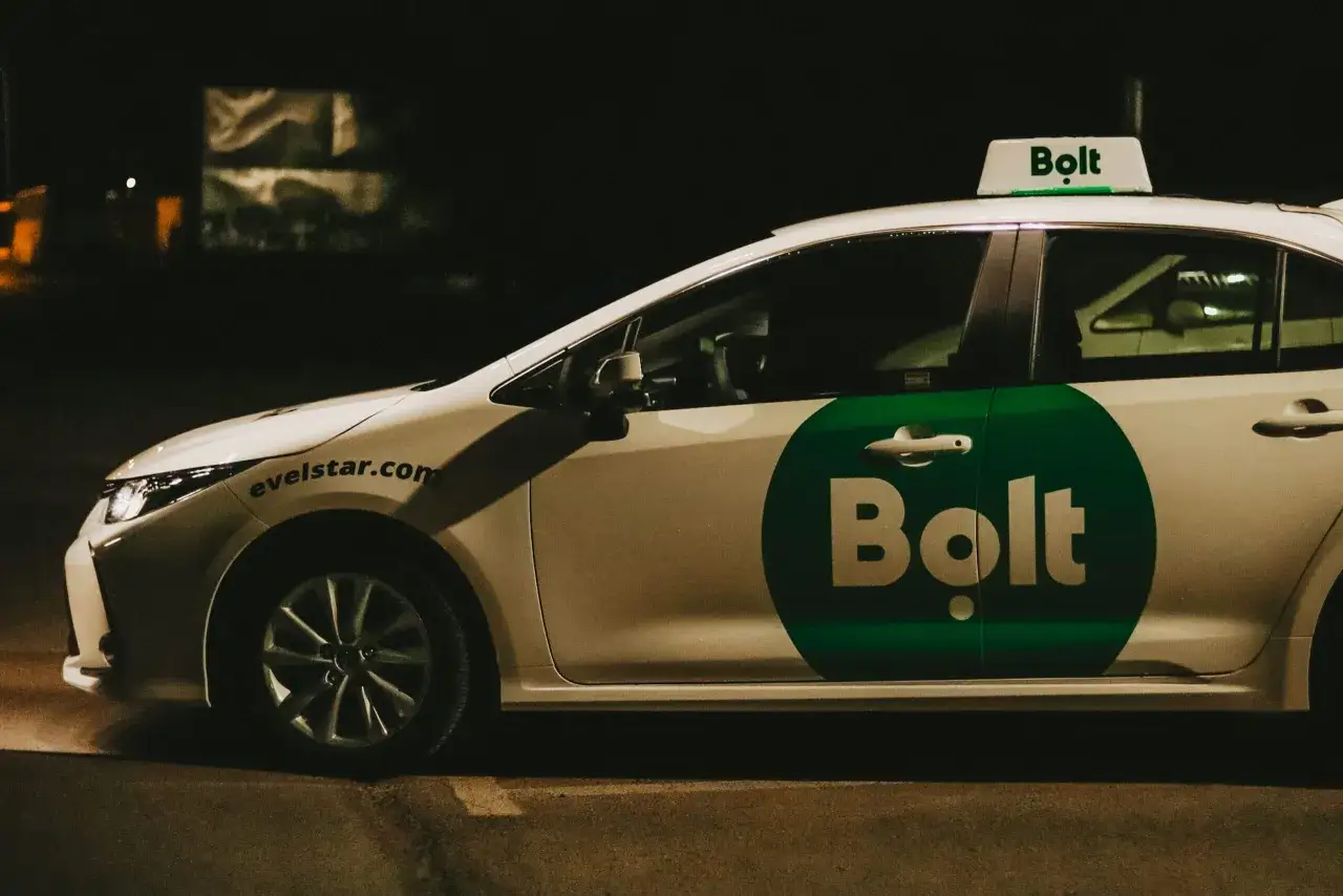 Biały samochód z zielonym logo Bolt na drzwiach i na dachu. To auto do pracy w Bolt.