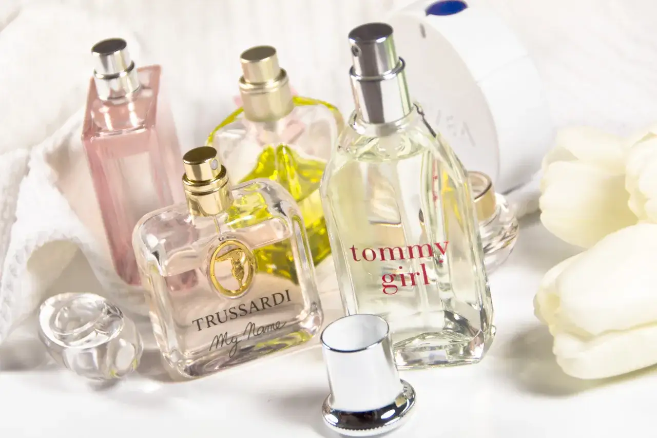 Mehrere Parfümflaschen, darunter Trussardi und Tommy Girl, auf weißem Handtuch mit weißen Tulpen.