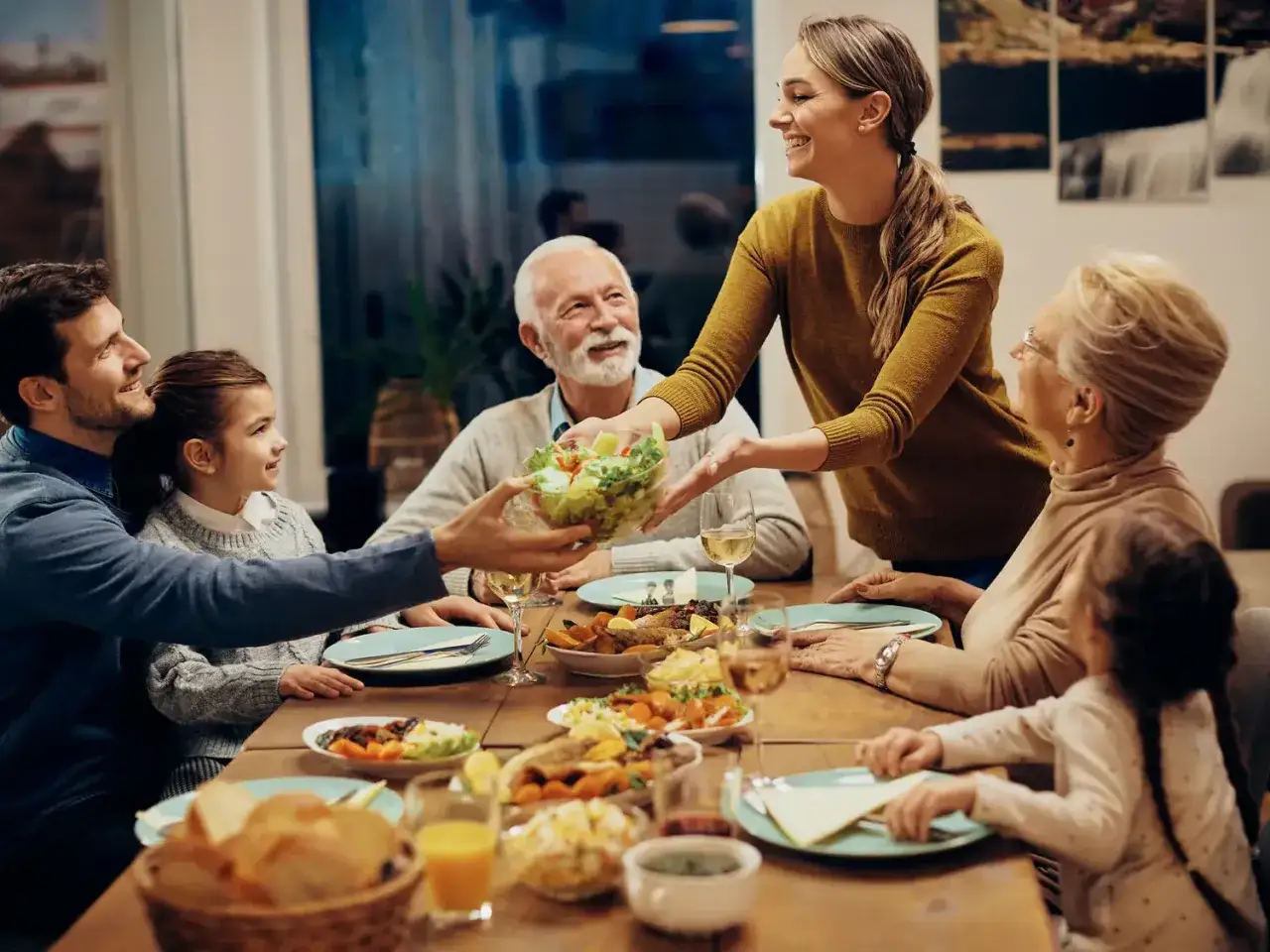 Une famille partage un repas joyeux. La mère sert la salade, et tout le monde sourit. C'est un moment de partage, alors pourquoi ne pas mettre les coudes sur la table ?