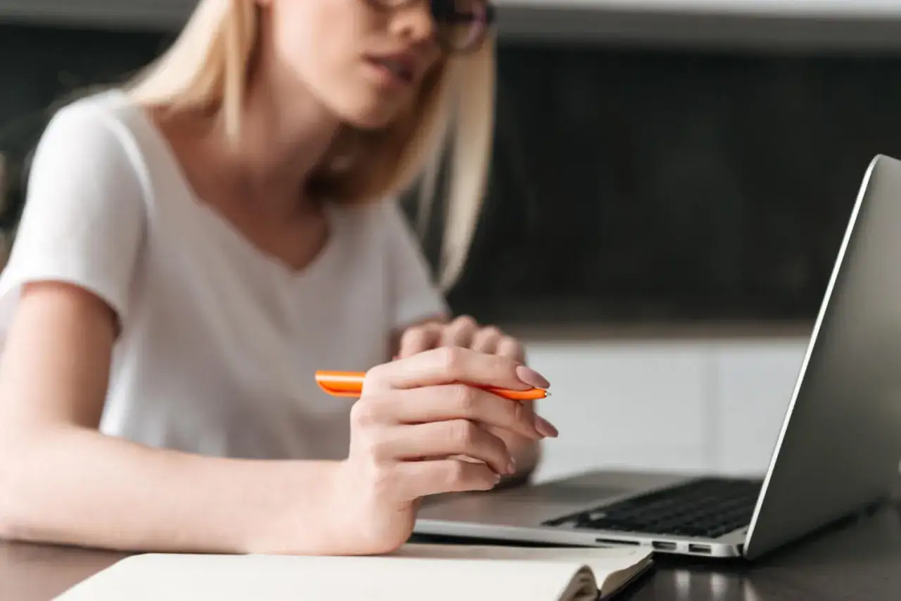 Kobieta w okularach pisze w notatniku, przygotowując przykładowe uzasadnienie wniosku o przyznanie pomocy zdrowotnej na okulary.