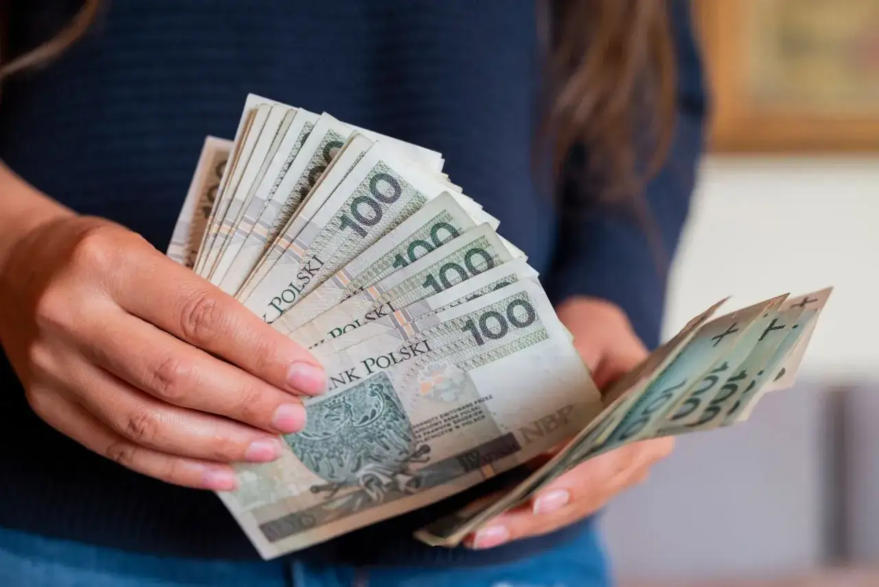 Dłonie trzymające stos banknotów 100 zł. Czy to przedpłata, czy zaliczka? Decyzja o płatności.