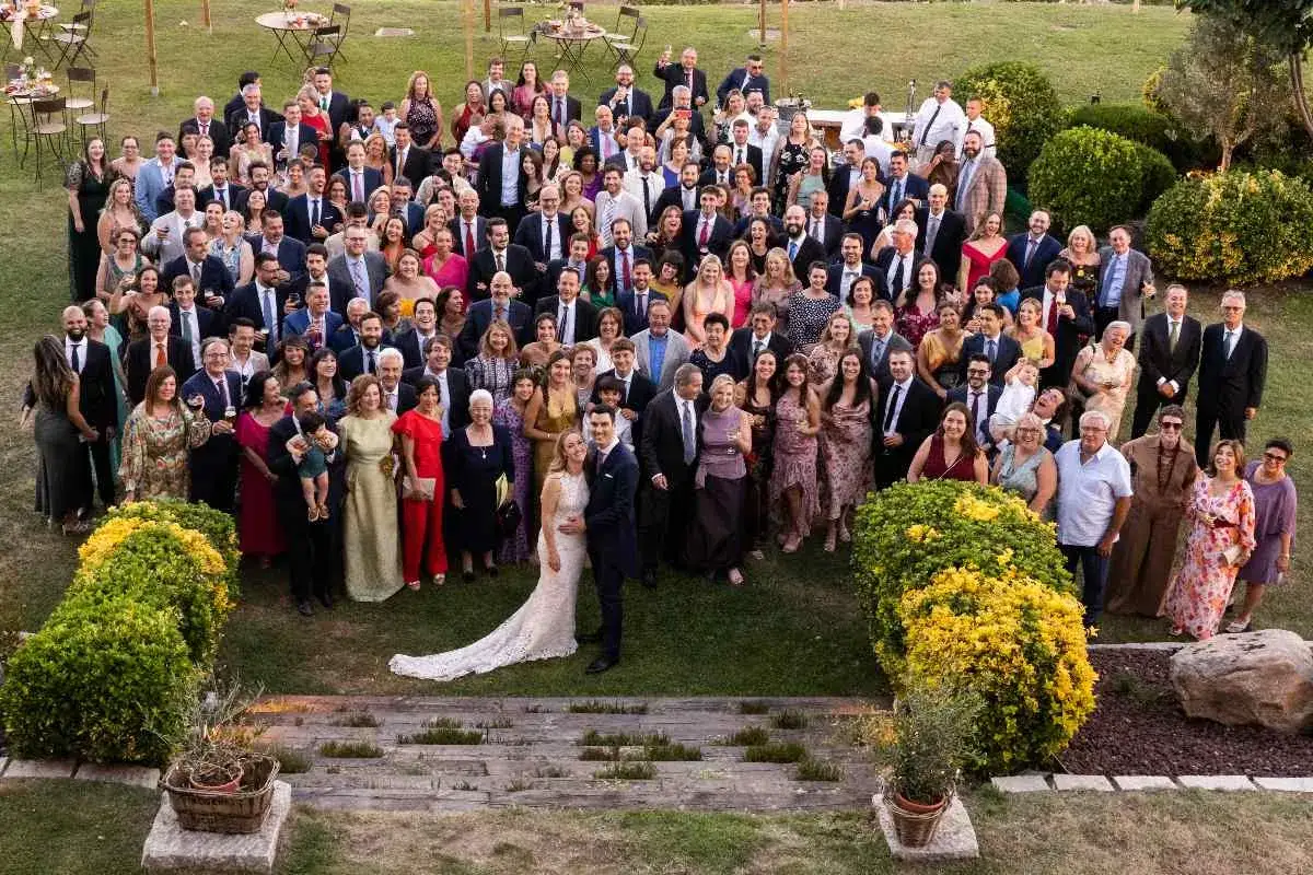 Una gran familia celebra una boda íntima al aire libre. Todos posan sonrientes para la foto grupal en un jardín verde.