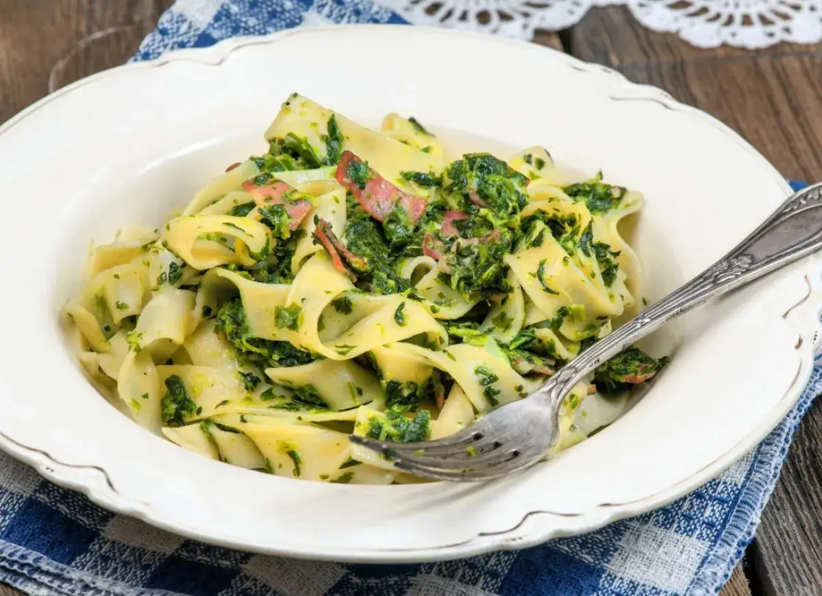 Pappardelle z boczkiem i szpinakiem, podane na białym talerzu, z widelcem.