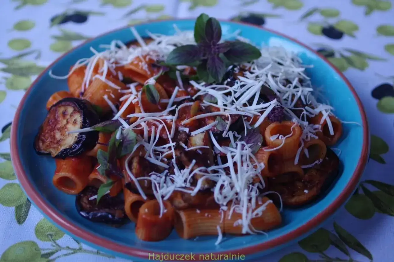 Makaron rigatoni z sosem pomidorowym, bakłażanem i startym serem, ozdobiony bazylią.