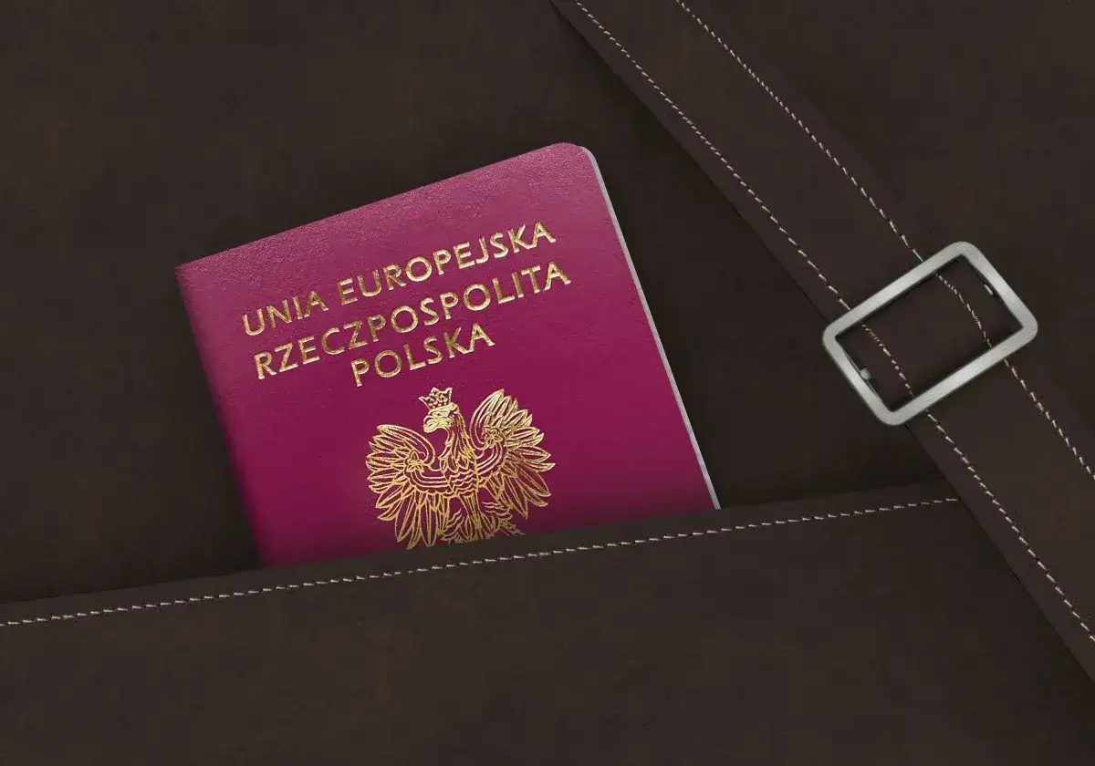 Nowy polski paszport w kolorze fuksji z godłem orła w złocie, schowany w brązowej skórzanej kieszeni.
