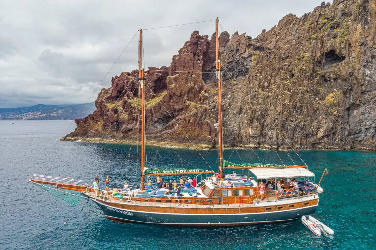 Segelschiff mit vielen Passagieren vor steiler Felsküste, ein Traum für Madeira Segeln.