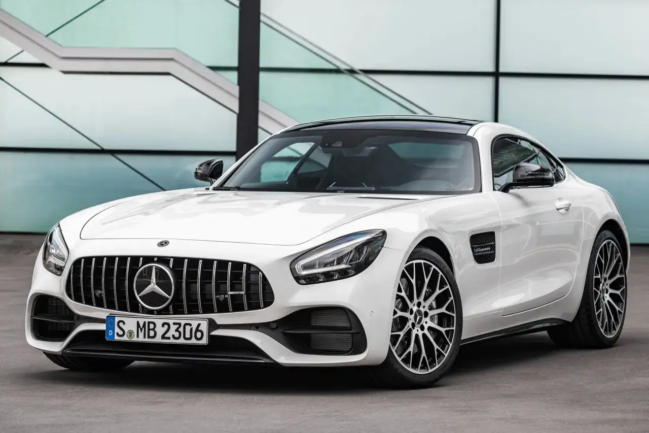 Biały Mercedes-AMG GTR z czarnym dachem i felgami, zaparkowany przed nowoczesnym budynkiem.