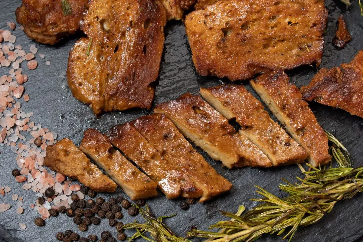 Seitan co to? Pokrojony w plastry, smażony seitan z przyprawami: różową solą, pieprzem i rozmarynem.
