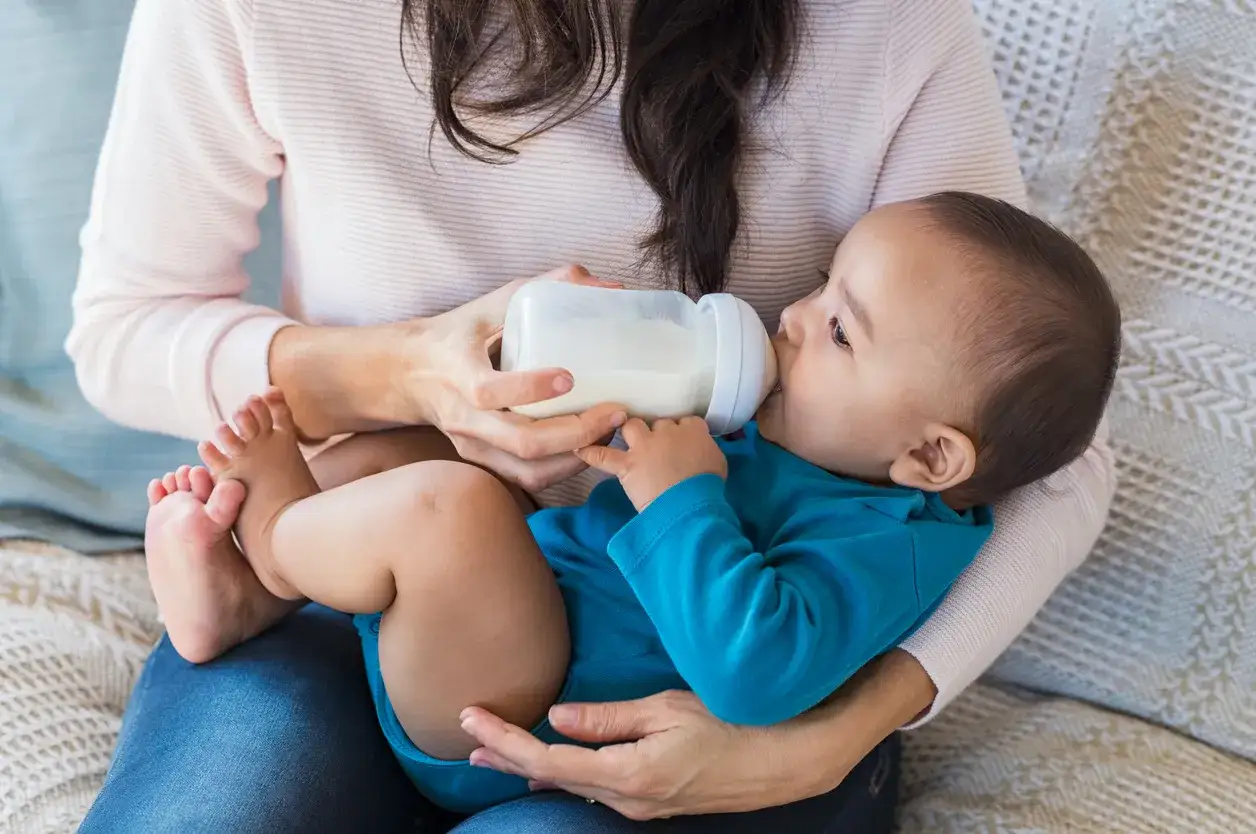 Mama karmi dziecko butelką. To przykład karmienia mieszanego, gdzie dziecko otrzymuje zarówno mleko matki, jak i mleko modyfikowane.