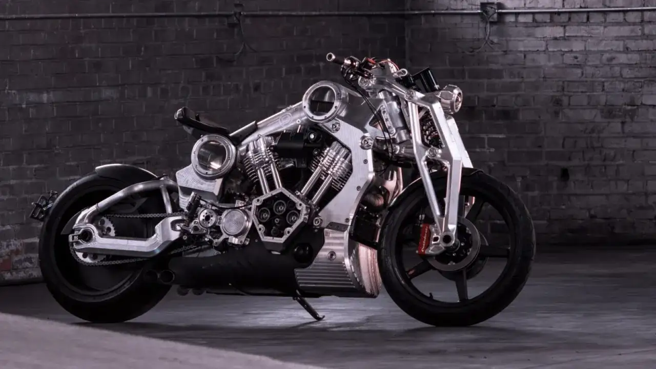 Wyjątkowy, lśniący motocykl, prawdopodobnie najdroższy motor na świecie, z masywnym silnikiem i detalami z polerowanego metalu, na tle ceglanej ściany.